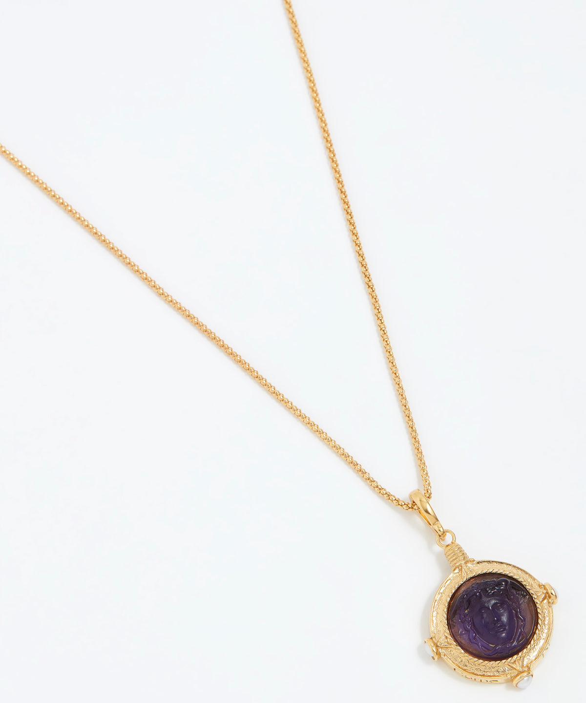Gold necklace with a purple stone pendant on a white background