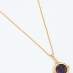 Gold necklace with a purple stone pendant on a white background