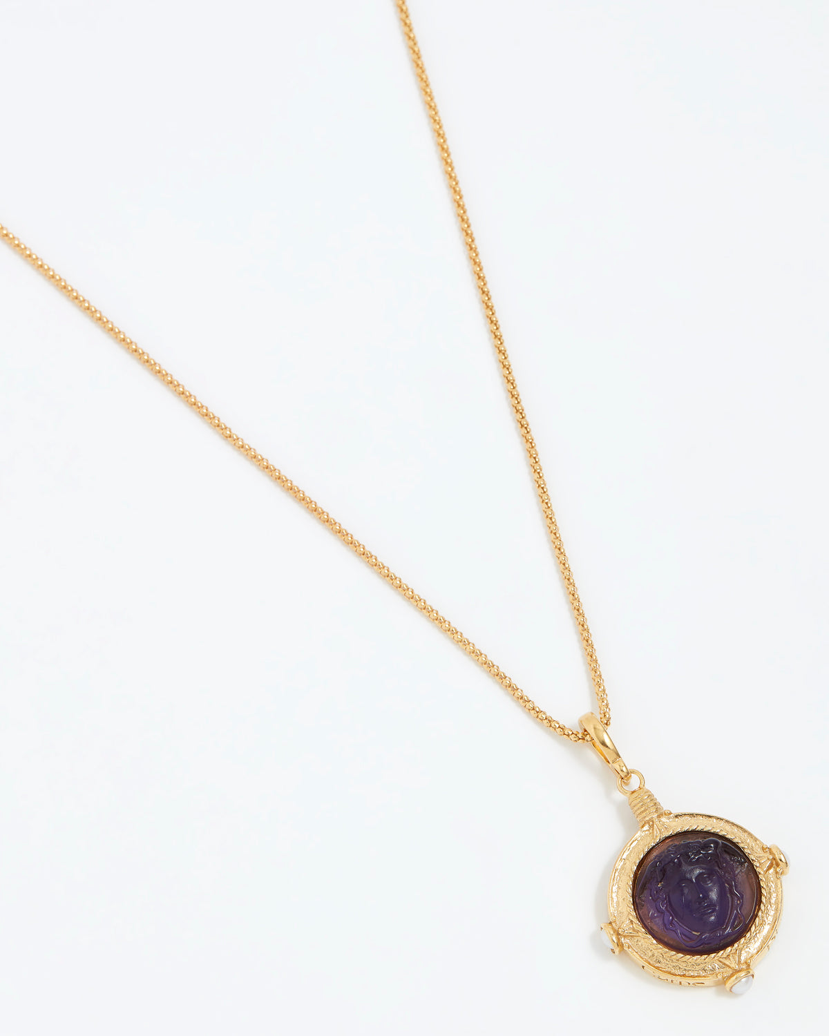 Gold necklace with a purple stone pendant on a white background