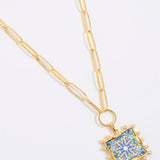 Decorative pendant with blue and gold design on a square tile with mini pearl edging  hung from a chinky gold chain on a white background