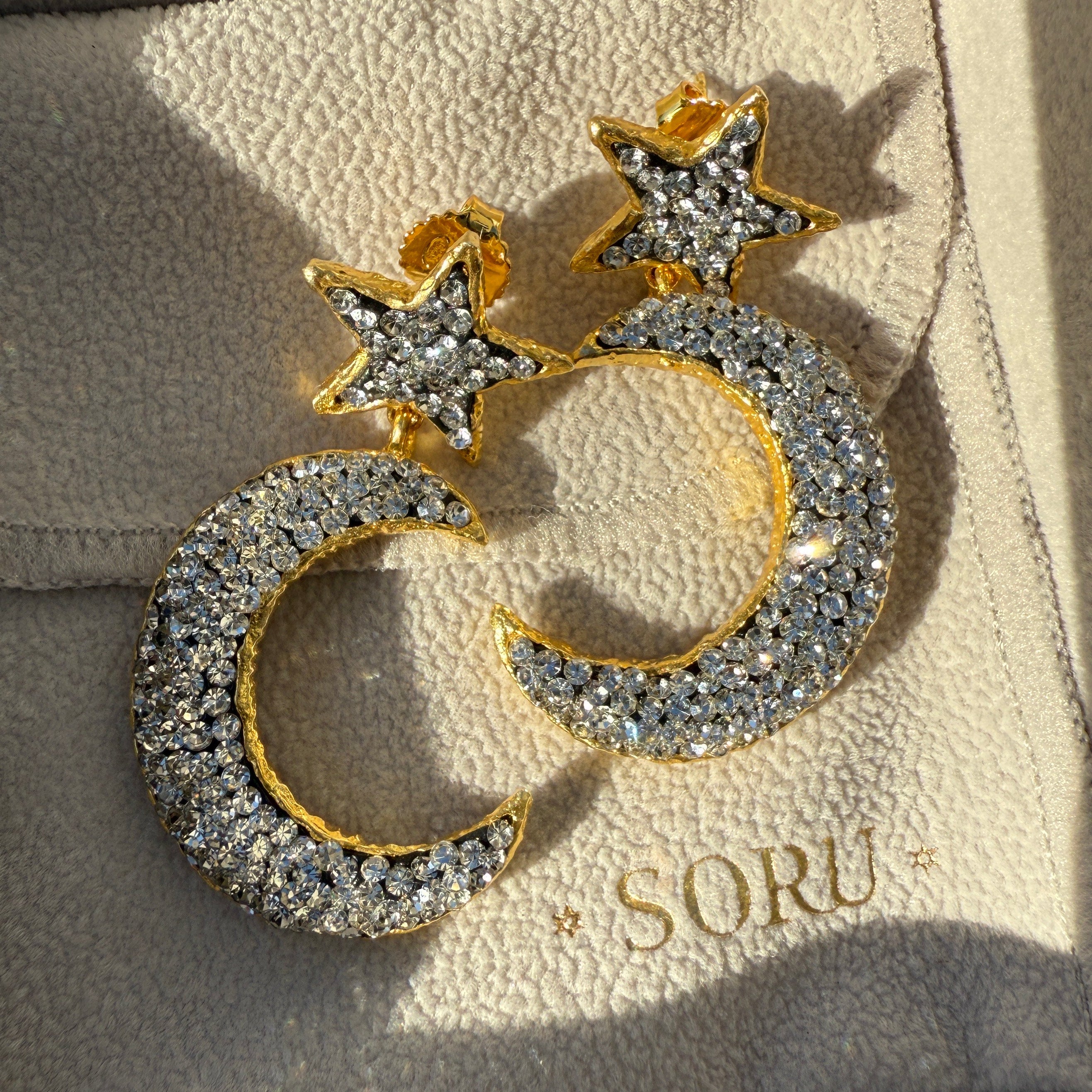 Gold and silver moon and star earrings on a SORU branded box.