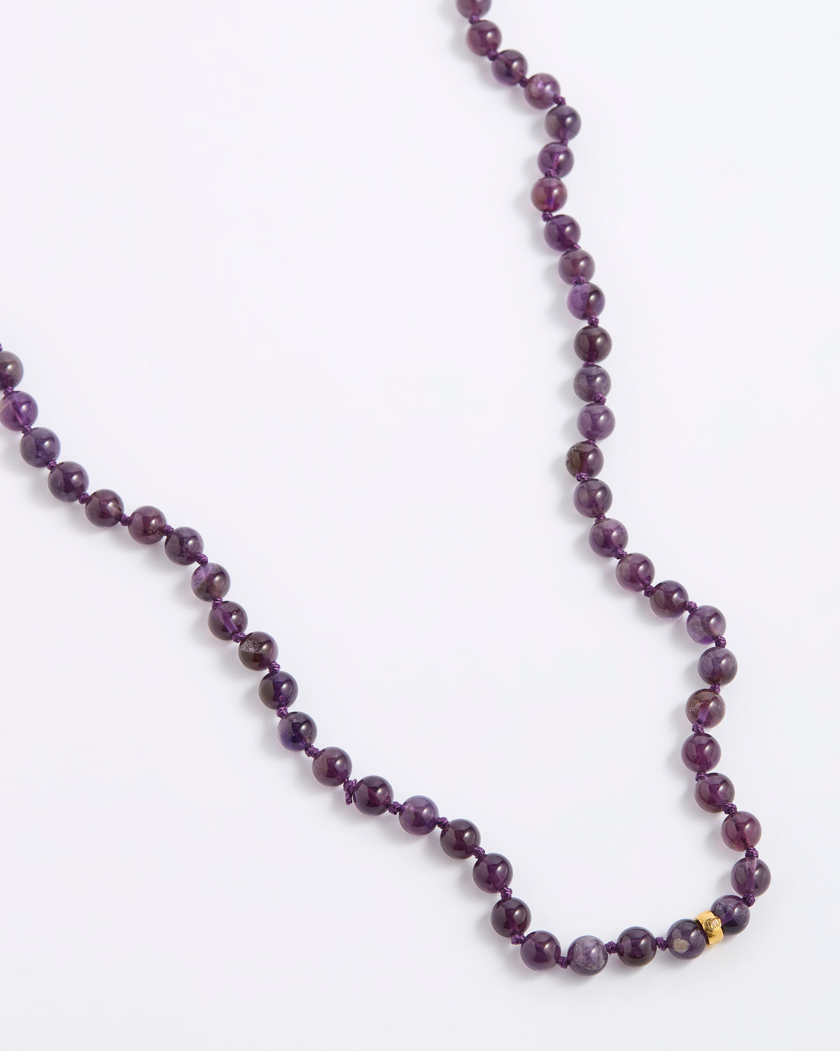 A beaded necklace made of dark purple, round gemstone beads with a small gold spacer bead, displayed on a clean white background.