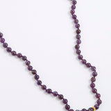 A beaded necklace made of dark purple, round gemstone beads with a small gold spacer bead, displayed on a clean white background.