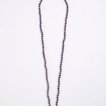 A long beaded necklace made of small dark purple faceted beads, laid flat on a plain white background.