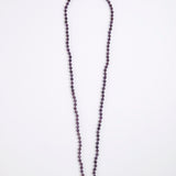 A long beaded necklace made of small dark purple faceted beads, laid flat on a plain white background.