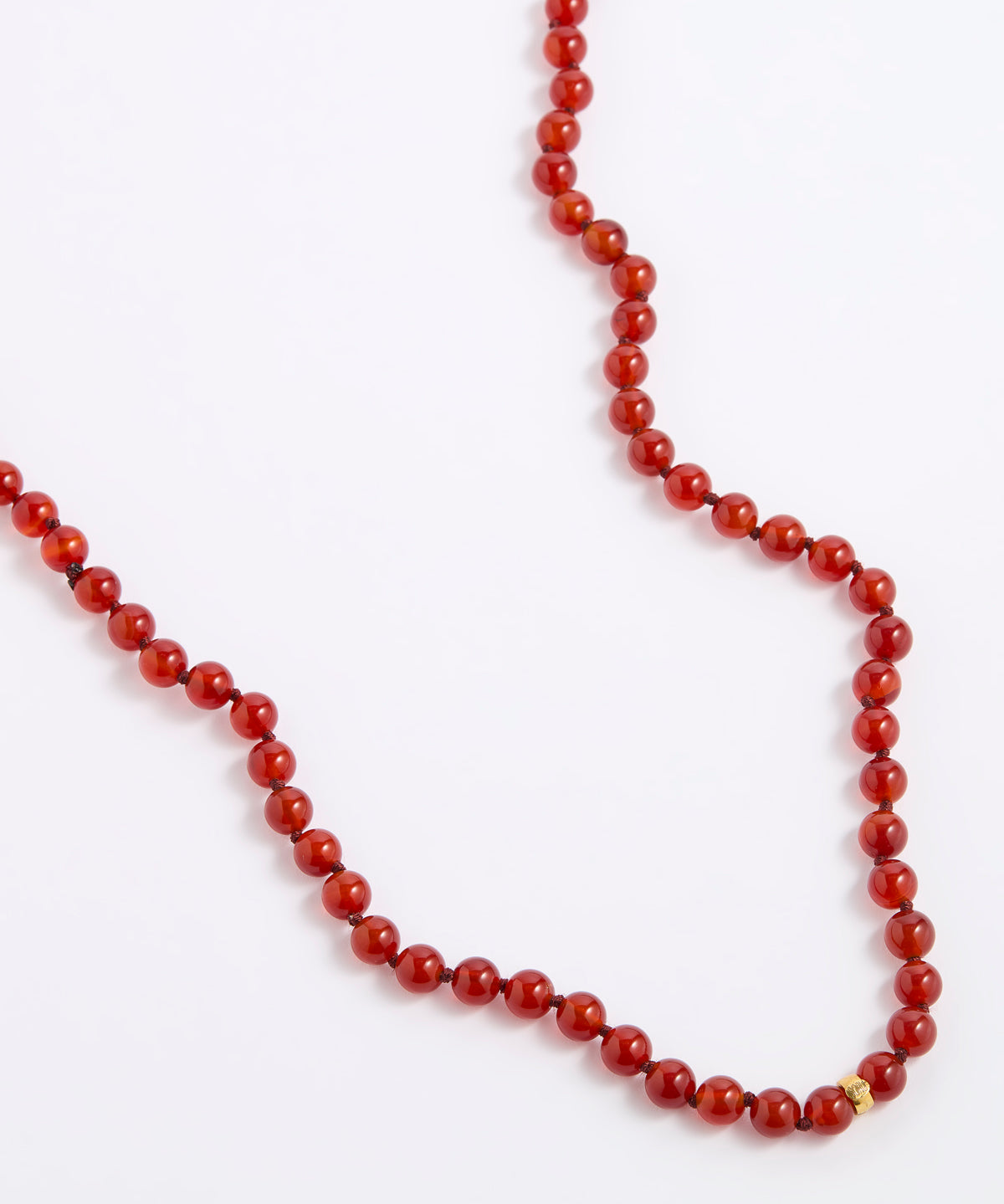 A red beaded necklace made of polished round beads, laid out on a plain white background.