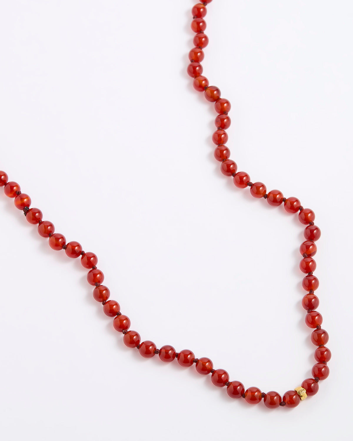A red beaded necklace made of polished round beads, laid out on a plain white background.