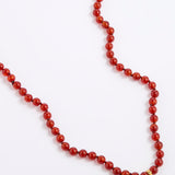 A red beaded necklace made of polished round beads, laid out on a plain white background.