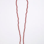A long beaded necklace made of small round red beads, laid flat on a plain white background.