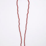 A long beaded necklace made of small round red beads, laid flat on a plain white background.