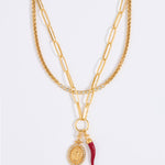 Gold chain necklace set with red cornicello and crystal pendant charms on a white background