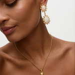 Close-up of a woman wearing gold earrings and necklace on a neutral background