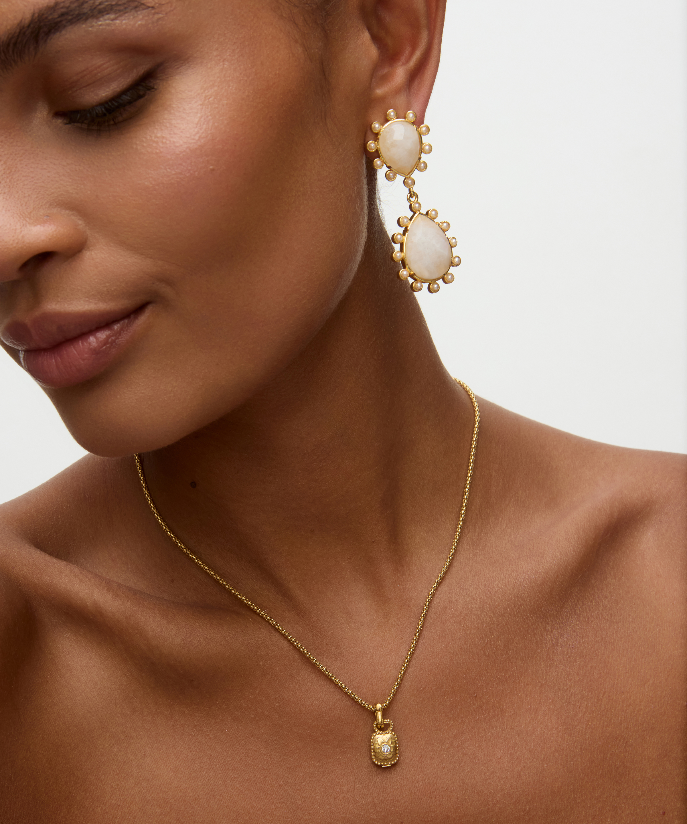 Close-up of a woman wearing gold earrings and necklace on a neutral background