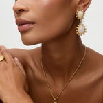 Close-up of a model wearing gold gold earrings with teardrop shaped moonstones and small pearls on  white background earrings and necklace against a neutral background