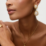 Close-up of a model wearing gold gold earrings with teardrop shaped moonstones and small pearls on  white background earrings and necklace against a neutral background