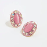 Product shot of Soru Jewellery large pink stud earrings surrounded by crystals on a white background