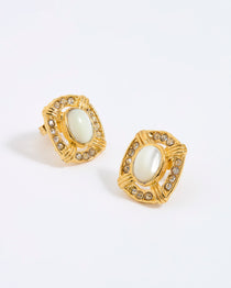 Gold earrings with central mother of pearl stone surrounded by small clear crystals,  on a light gray background