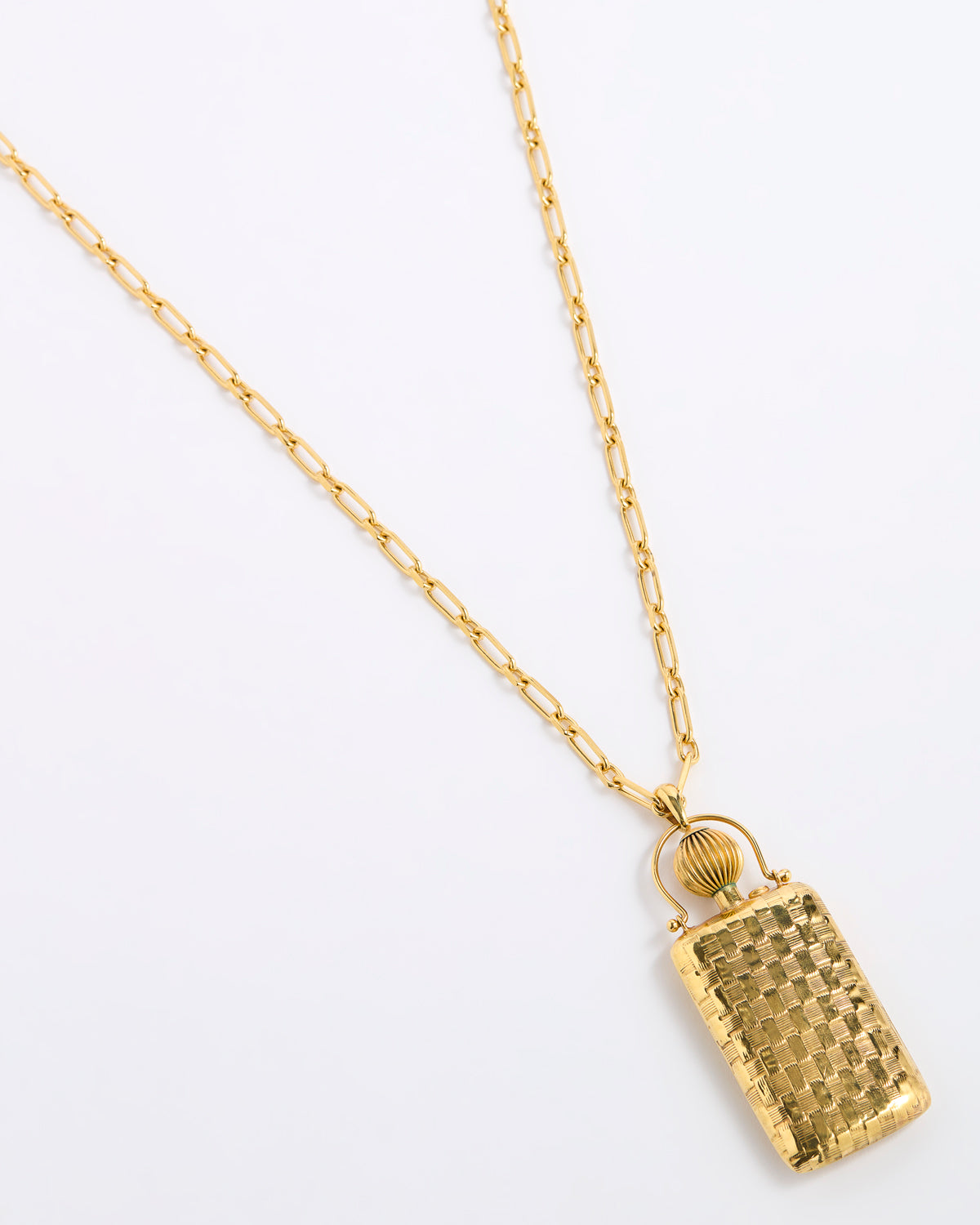 A gold pendant necklace featuring a textured, rectangular handbag-shaped charm with a small gold ring detail above it, suspended from a delicate gold chain on a plain white background.