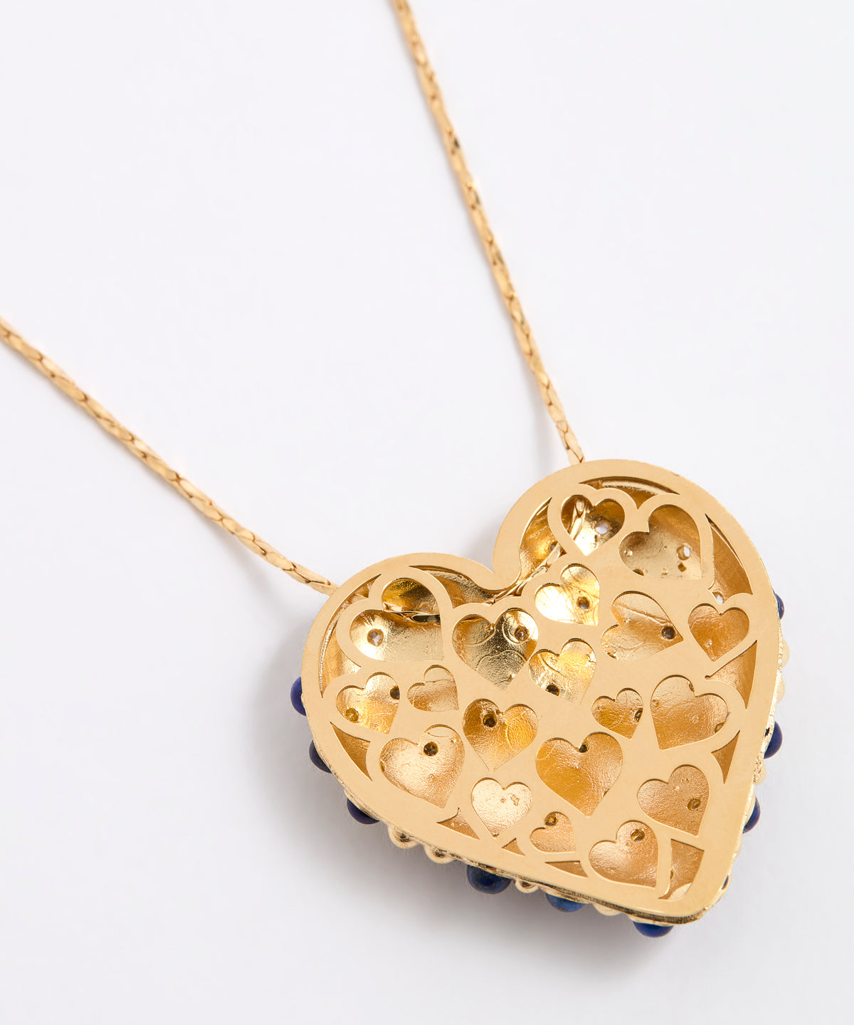 Reverse image of a gold heart-shaped pendant necklace with intricate cutout heart patterns, featuring small dark blue bead accents along the bottom edge, shown on a white background.