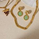 Gold necklace with green gemstone earrings on a beige fabric background