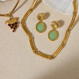 Gold necklace with green gemstone earrings on a beige fabric background