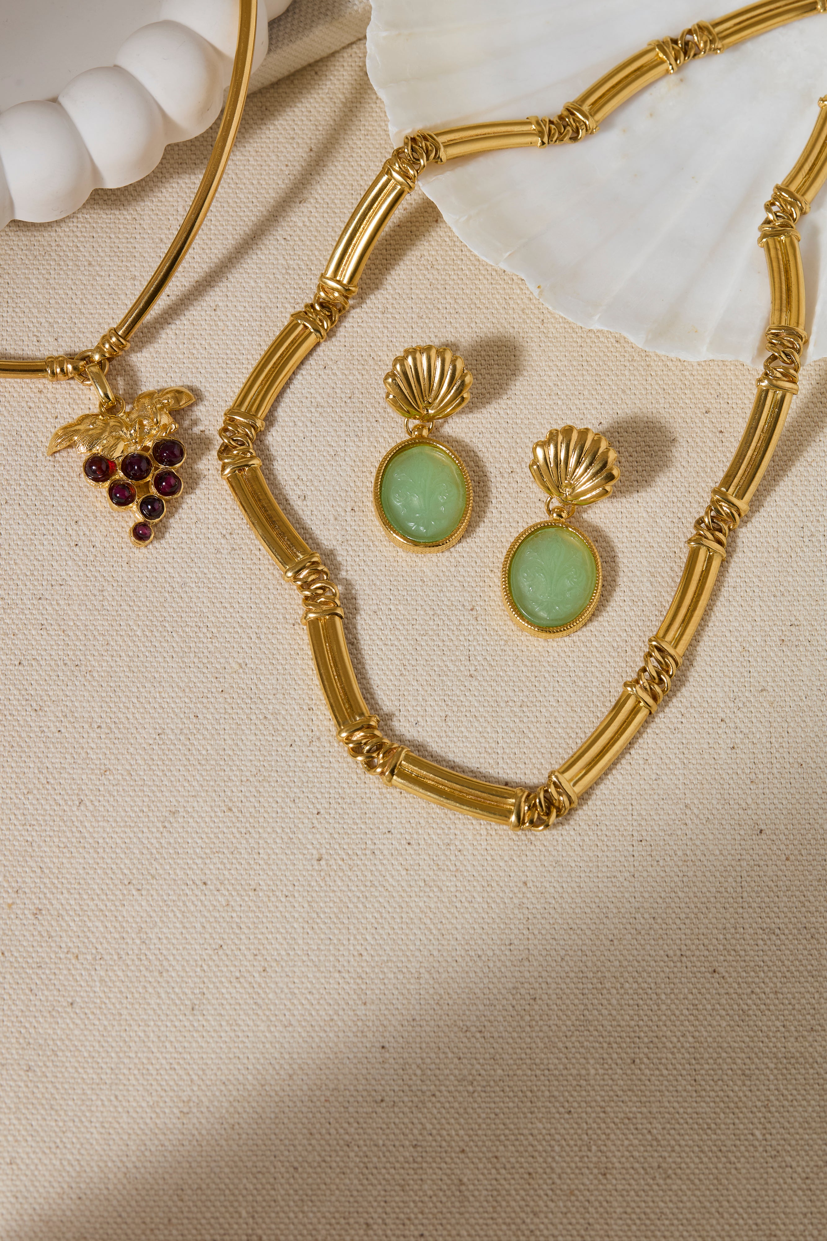 Gold necklace with green gemstone earrings on a beige fabric background