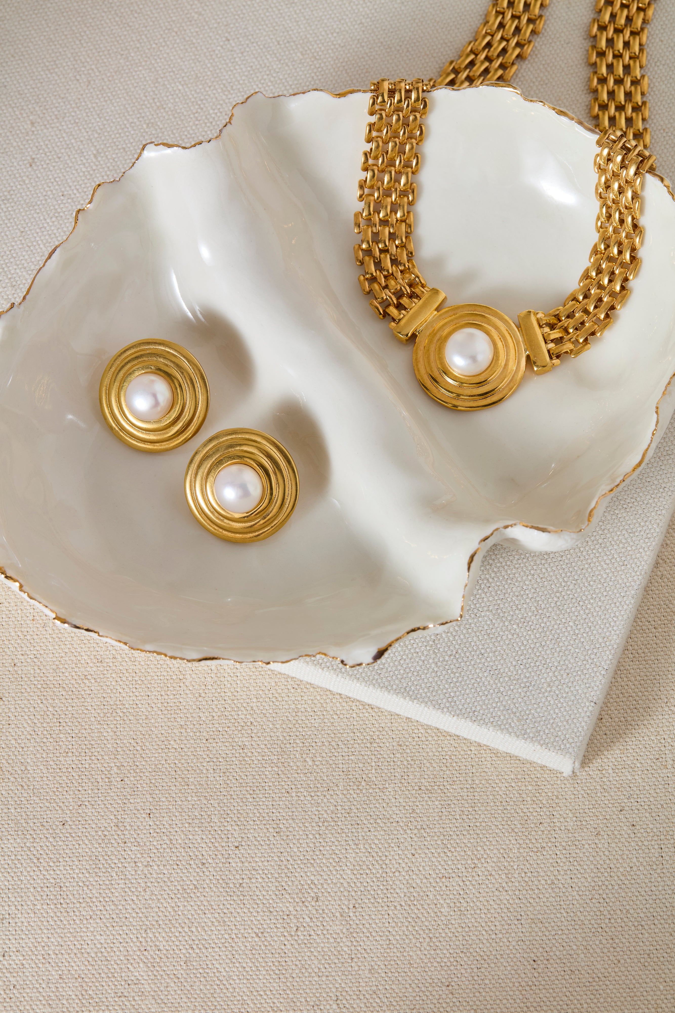 Gold necklace and earrings on a white shell with a beige background