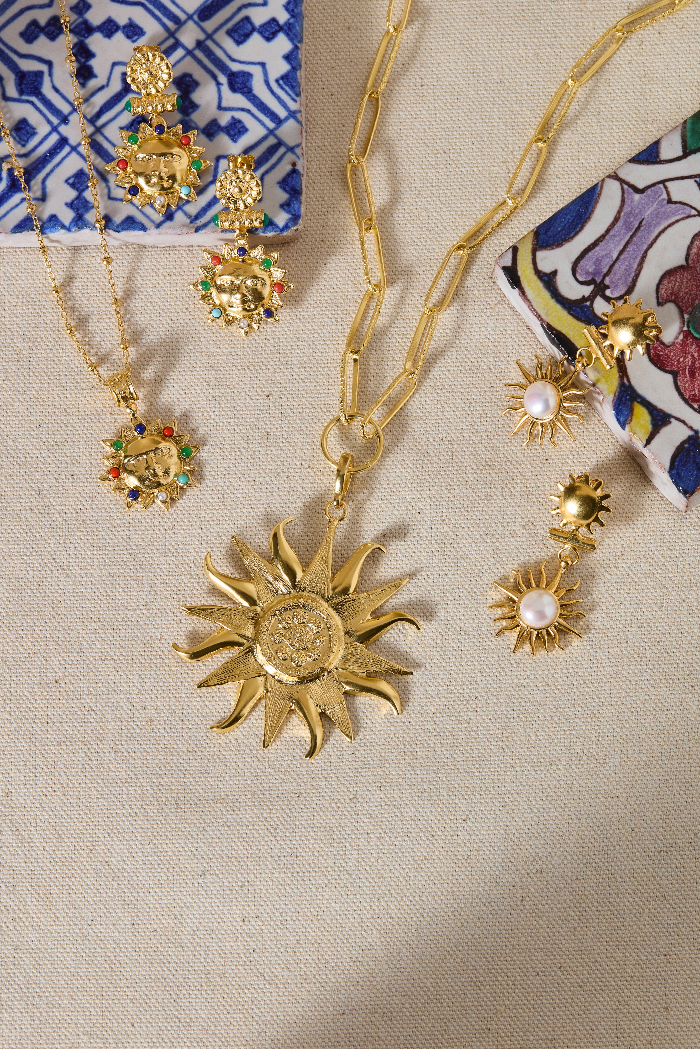 Gold jewelry set with sun-shaped pendant and floral earrings on a textured surface.