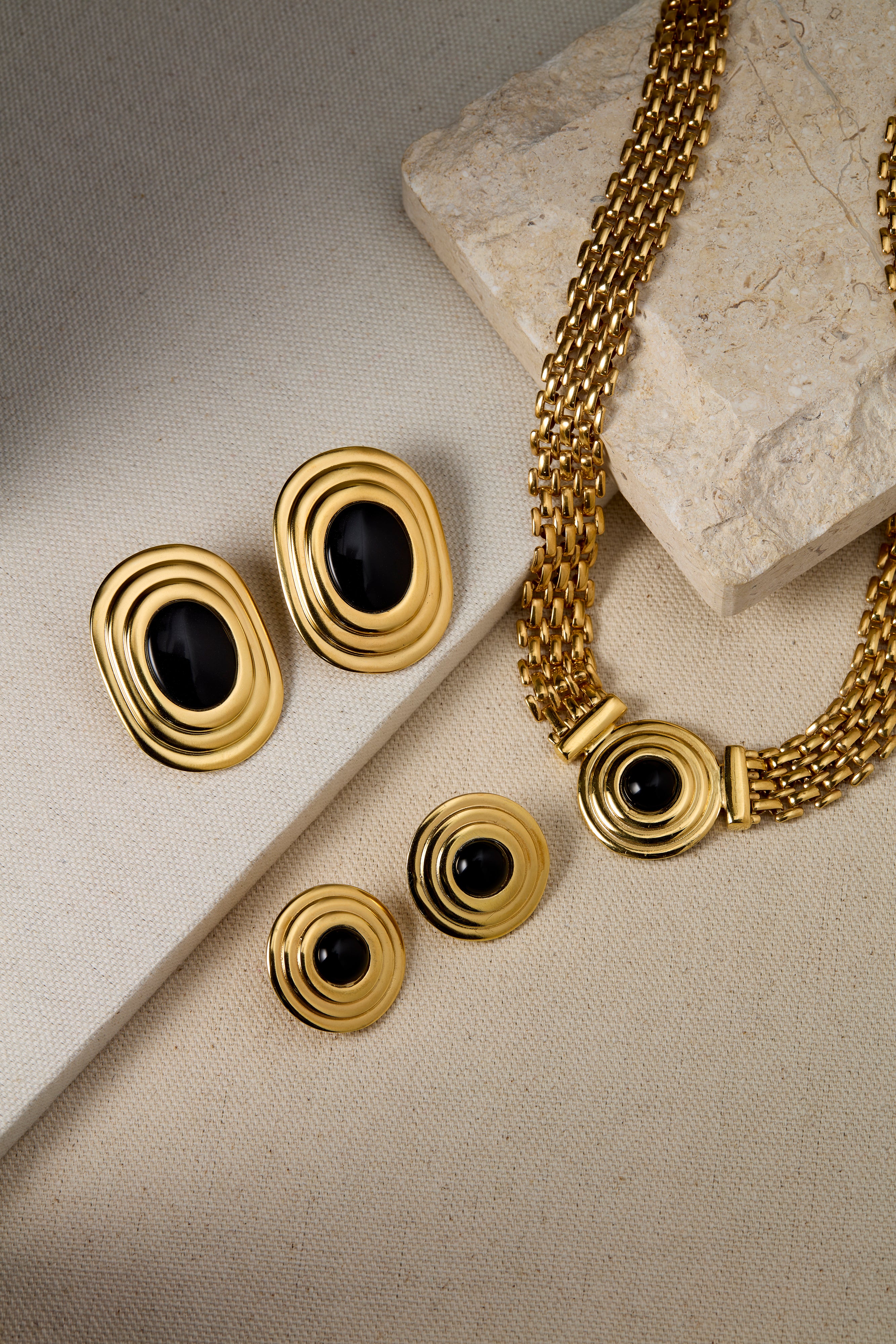 Gold jewelry set with black stones on a textured surface