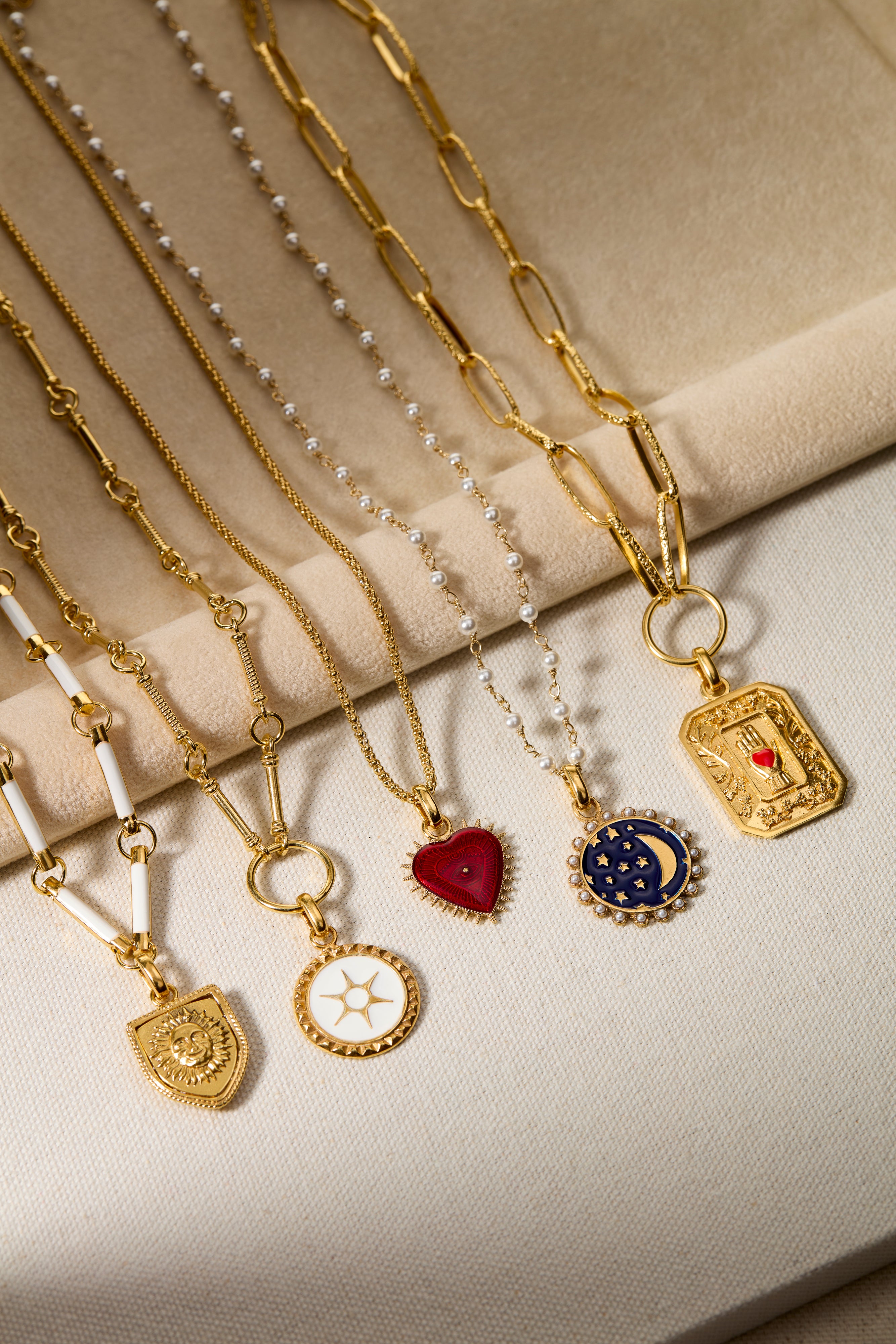 Collection of gold necklaces with various pendants on a beige surface