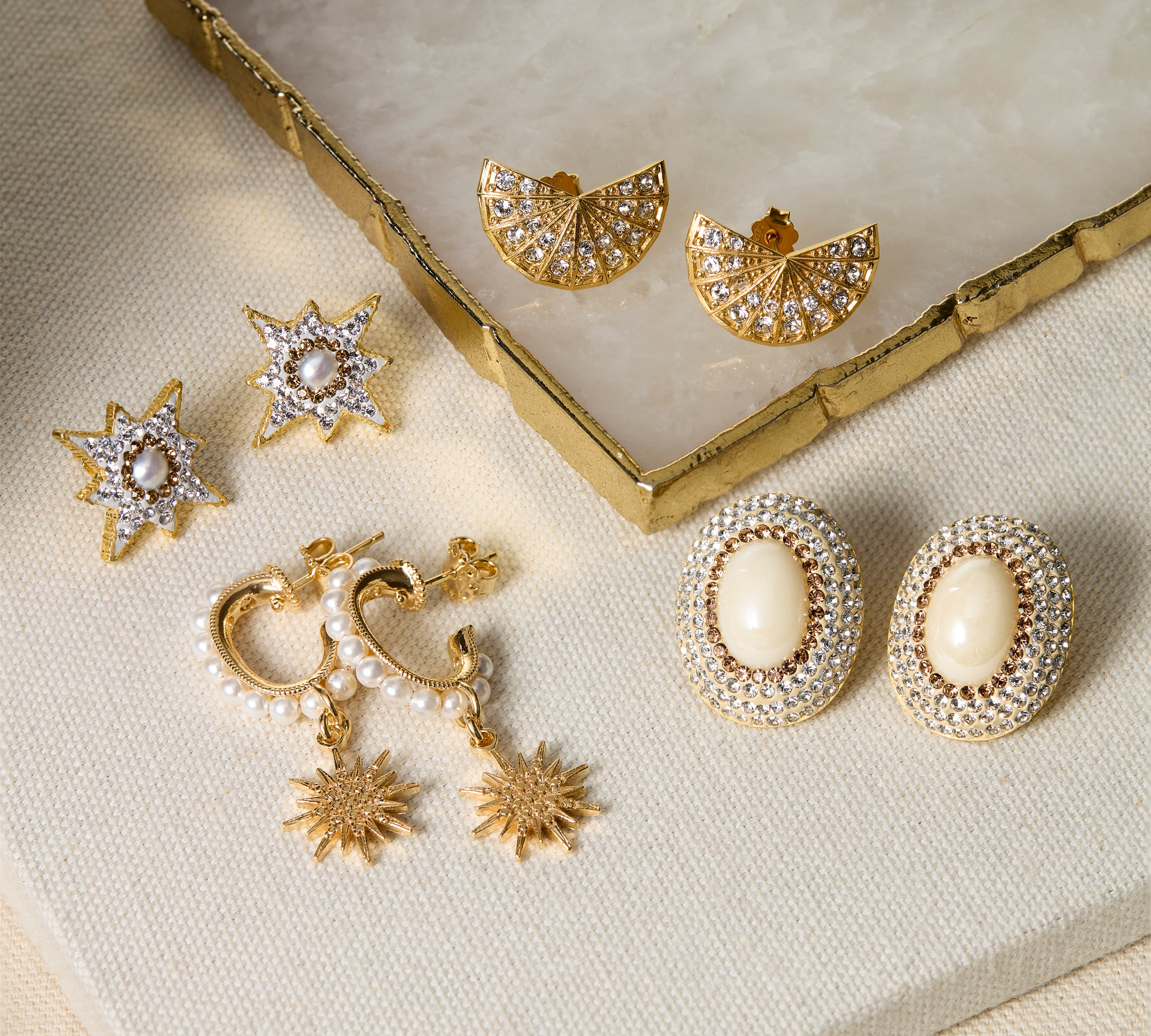 Set of gold and pearl earrings on a textured surface