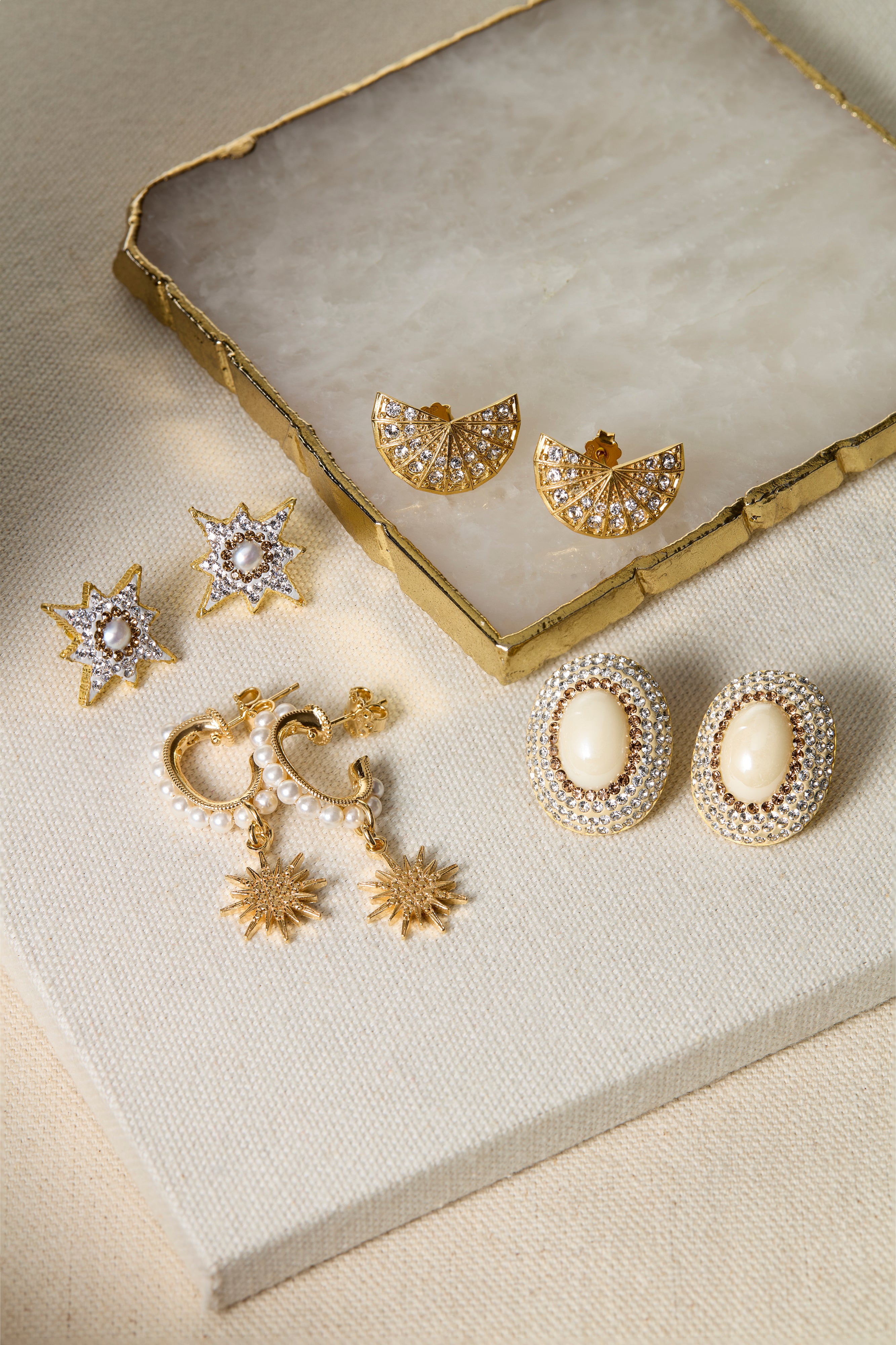 Set of gold and pearl earrings on a textured surface