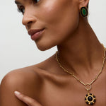 Model wearing matching gold earrings and ring with green malachite stone and black enamel  on a white background. 
