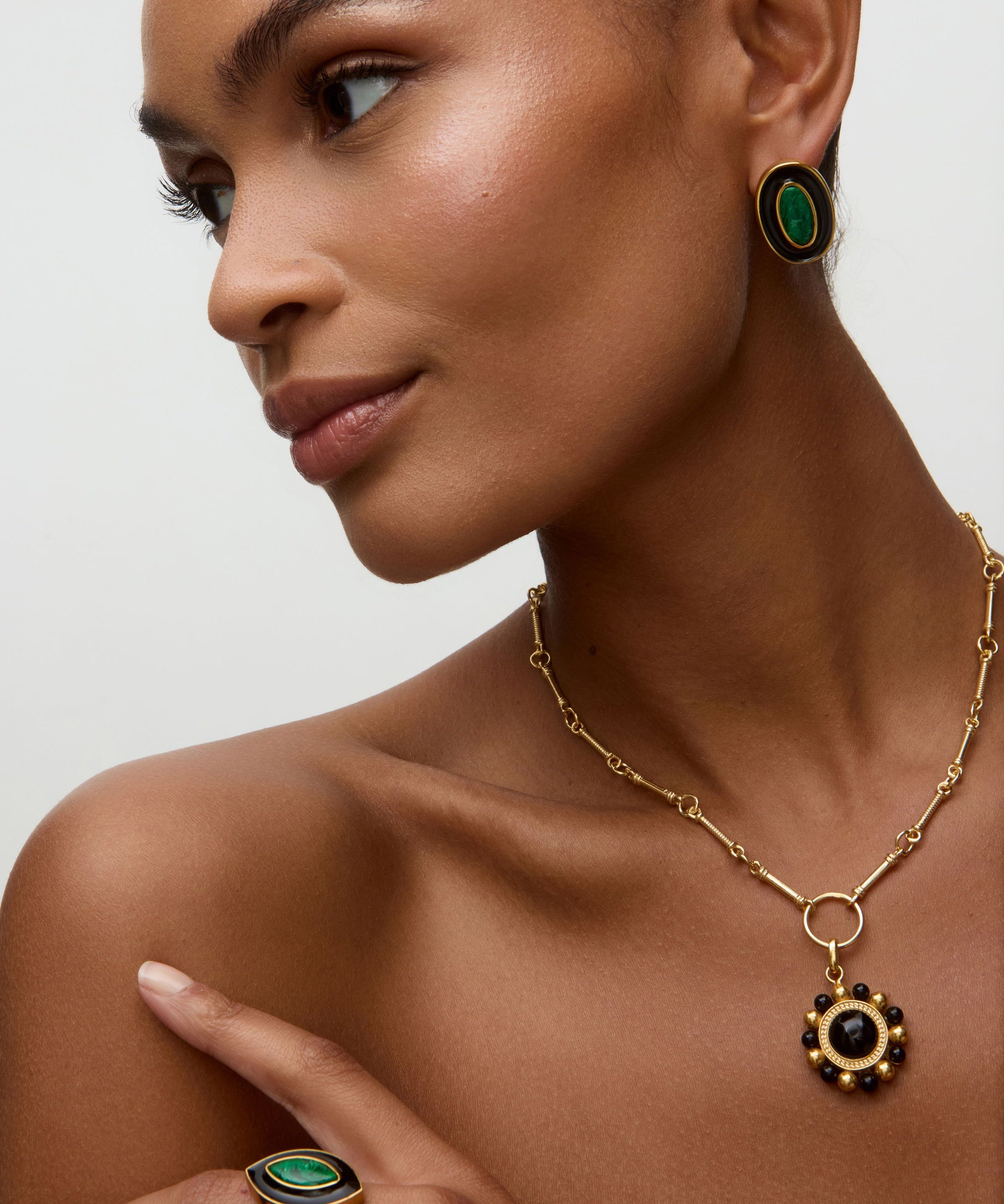 Model wearing matching gold earrings and ring with green malachite stone and black enamel  on a white background. 
