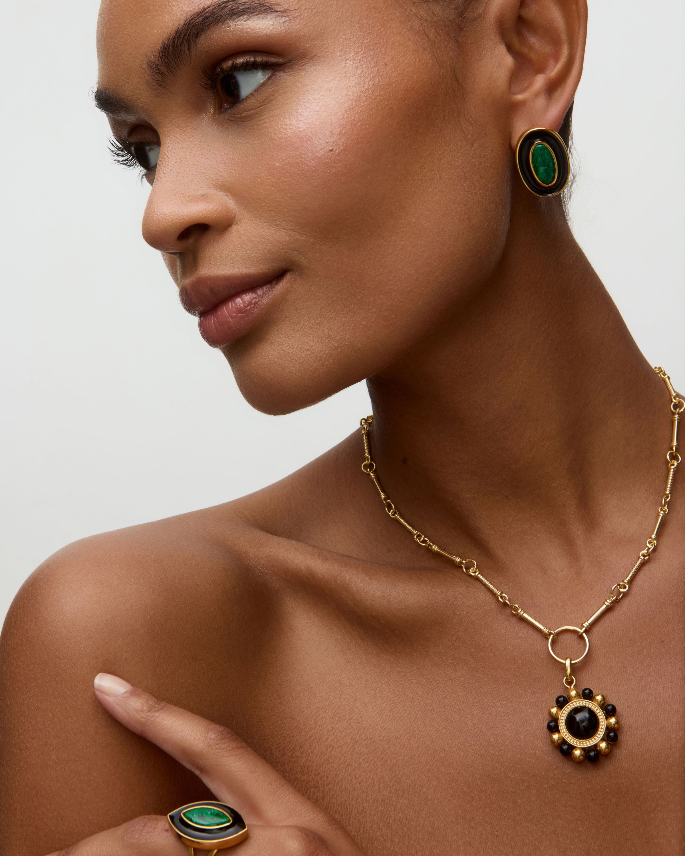 Model wearing matching gold earrings and ring with green malachite stone and black enamel  on a white background. 