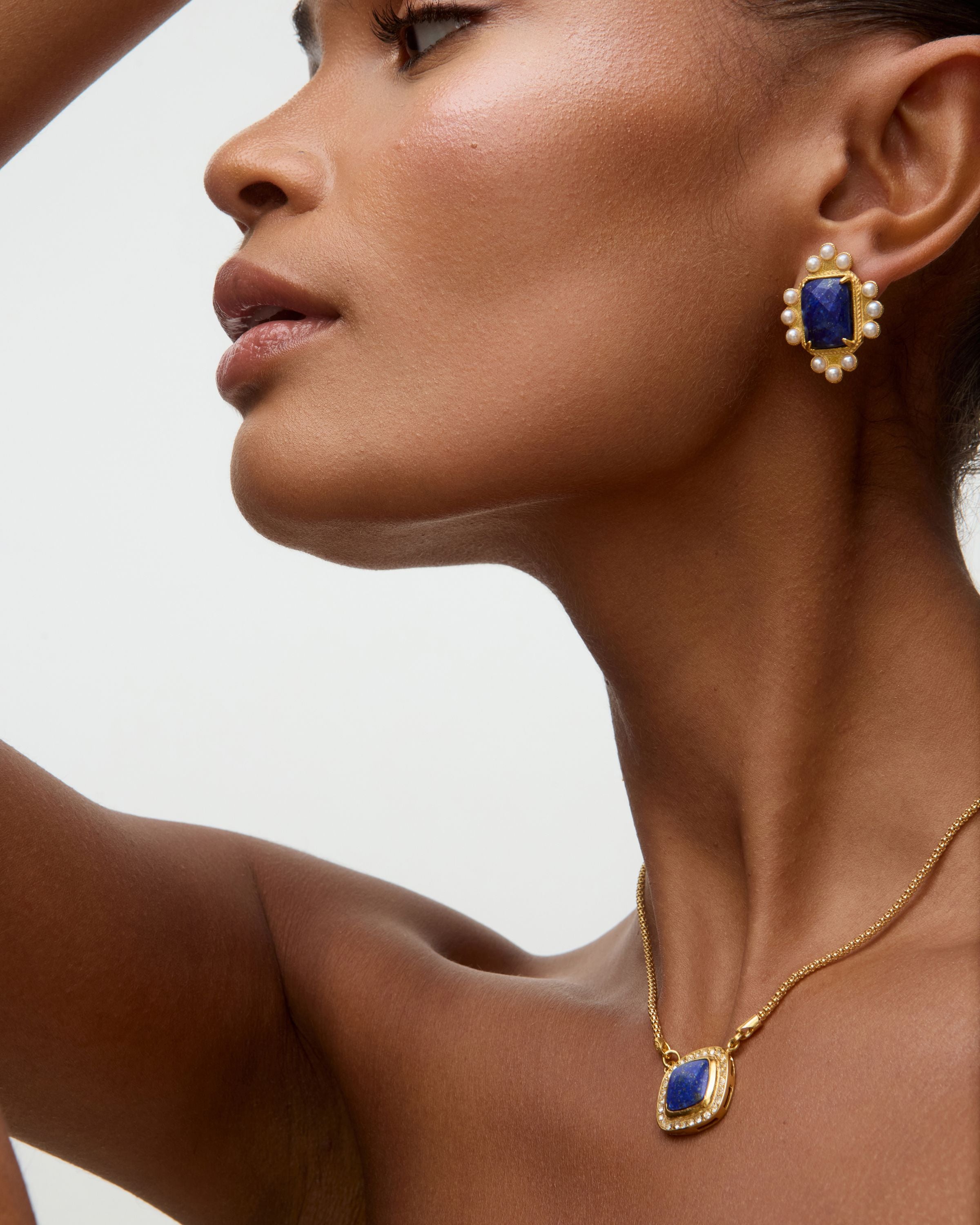 Side view of model shot of gold earrings featuring lapis central stone and embellished with pearl accents on a white background and gold necklace