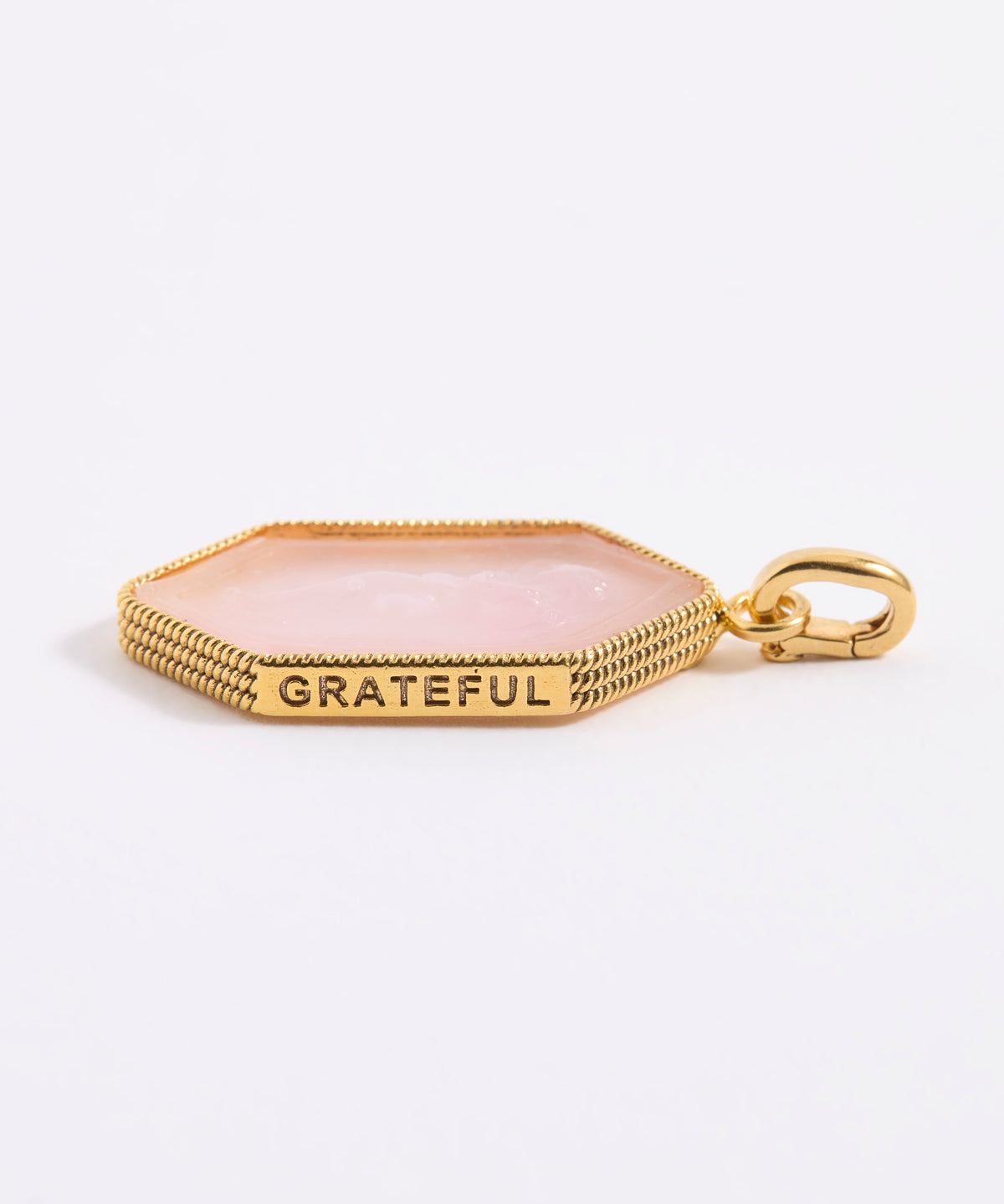 Gold charm with 'GRATEFUL' engraving on a light pink stone background