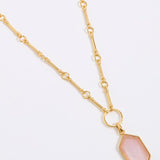 Gold necklace with a pink pendant on a light gray background
