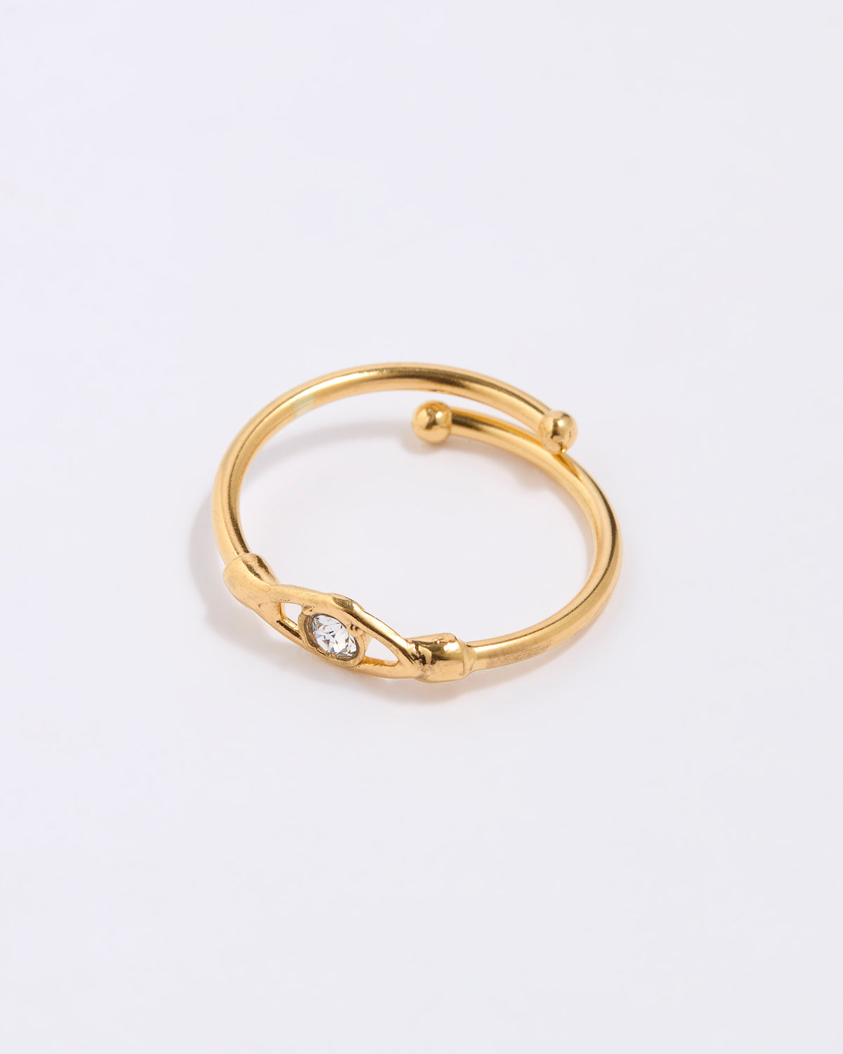 Gold coloured ring with a clear crystal at the centre of an evil eye on a light gray background