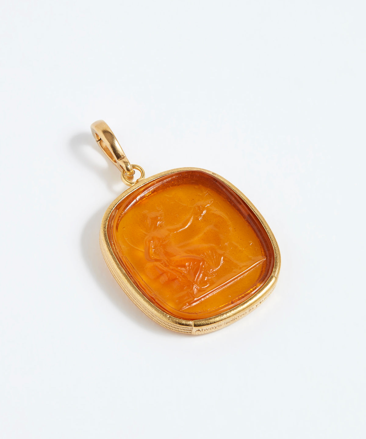 Gold pendant with an amber-colored stone featuring a engraved design on a white background