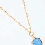 Gold necklace with a blue pendant on a white background
