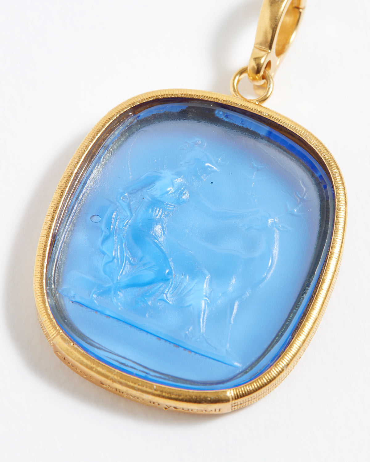 Gold pendant with a blue stone featuring an engraved design on a white background