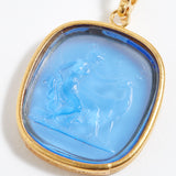 Gold pendant with a blue stone featuring an engraved design on a white background
