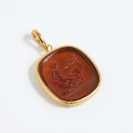 Gold pendant with a brown stone featuring an engraved design on a white background