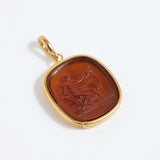 Gold pendant with a brown stone featuring an engraved design on a white background