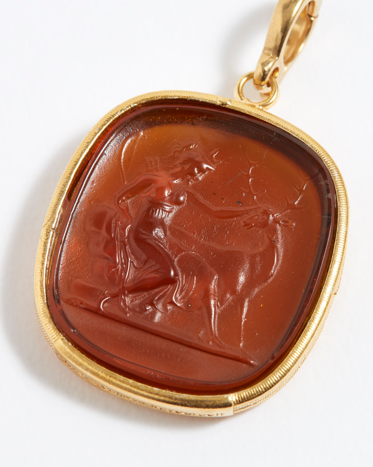 Gold pendant with a brown stone featuring a engraved design on a white background