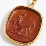 Gold pendant with a brown stone featuring a engraved design on a white background