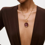 Gold necklace with a red pendant worn by a model against a neutral background