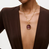 Gold necklace with a red pendant worn by a model against a neutral background