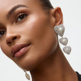 Close-up of a woman wearing heart-shaped earrings with a neutral background